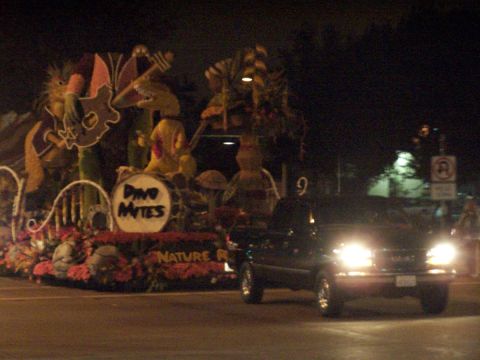 1990 Ford Bronco - A black pickup truck drives by a parade float decorated with cartoon dinosaurs and musical instruments.