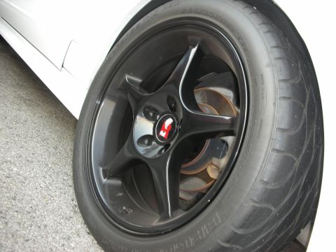 1998 Ford Crown Victoria - Close-up of a car's wheel and tire, showing a black five-spoke rim and a tire with text.