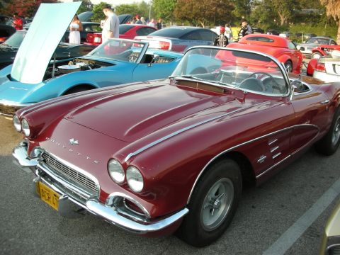1998 Ford Crown Victoria - A classic red Corvette convertible is parked at a car meet, with other vehicles visible in the background.