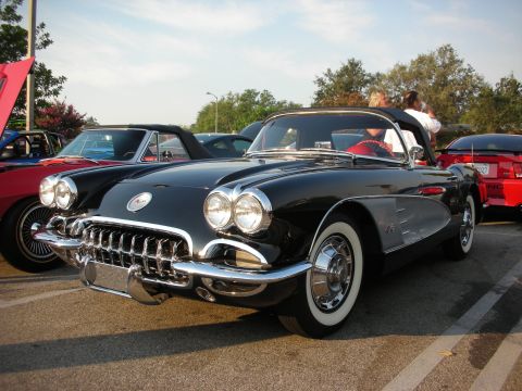 1998 Ford Crown Victoria - A classic black Chevrolet Corvette is parked at an outdoor car meet with other vehicles around it.
