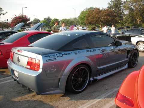 1998 Ford Crown Victoria - A modified Ford Mustang with racing decals is parked among other vehicles at a car show.
