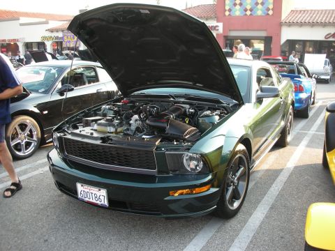 1998 Ford Crown Victoria - A green Ford Mustang is parked with its hood open, revealing the engine bay.