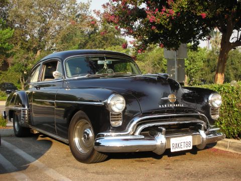 1998 Ford Crown Victoria - A classic black 1949 Oldsmobile 88 sedan is parked outdoors under a tree.