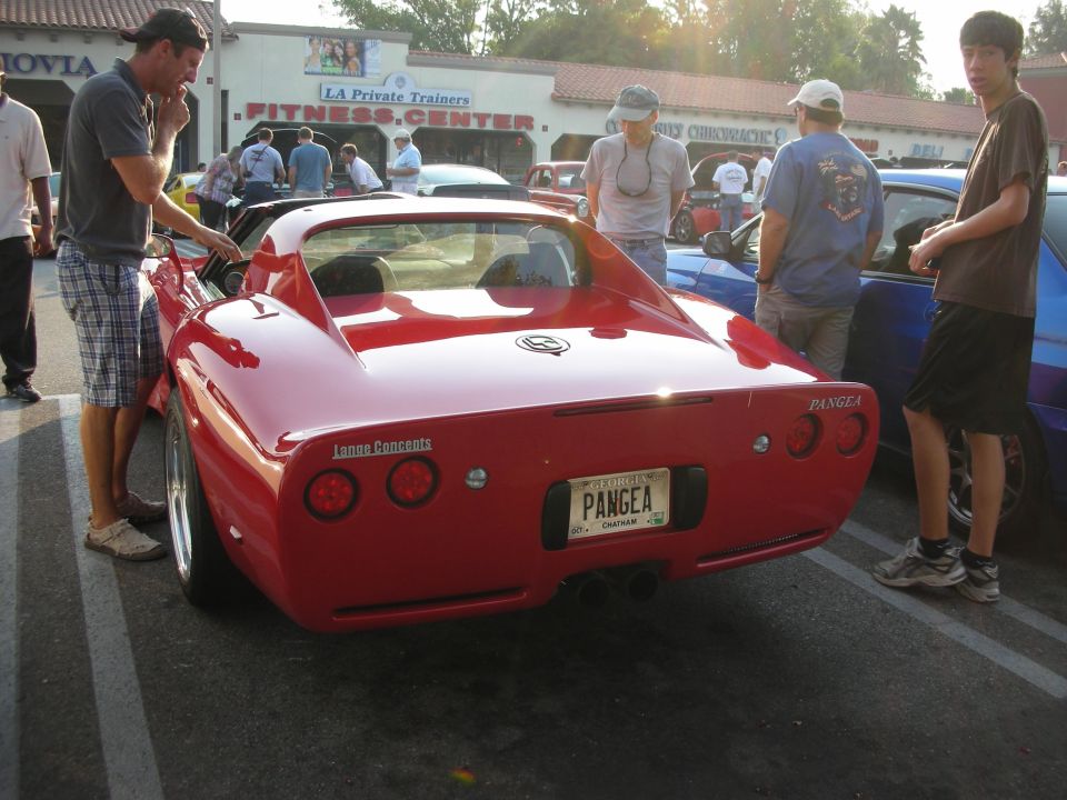 Red sports car with a custom license plate that says PANGAEA. People are standing around it