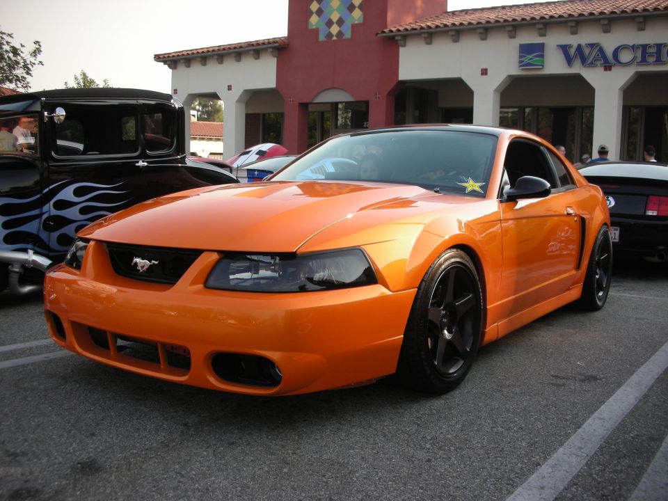Orange Ford Mustang coupe with black wheels and tinted headlights