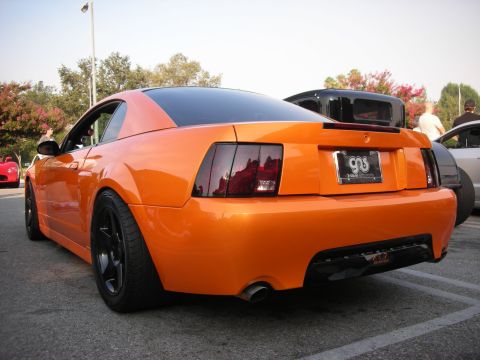 1998 Ford Crown Victoria - Rear view of an orange Ford Mustang with aftermarket wheels and tinted taillights.