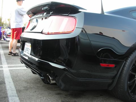 1998 Ford Crown Victoria - Rear view of a black Shelby Mustang at a car meet. A person stands to the left of the vehicle.