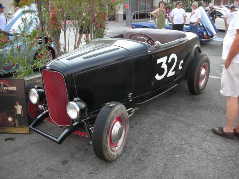 1998 Ford Crown Victoria - A black hot rod roadster with a red grille and white number 32 is parked outdoors with other vehicles and people around.
