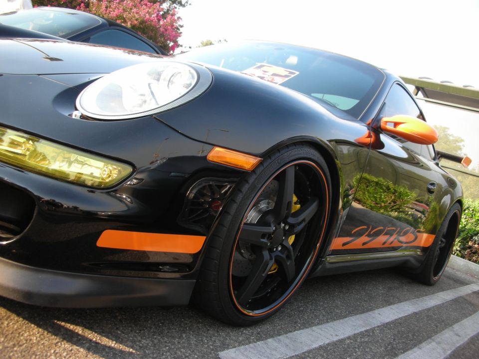 Black Porsche 911 with orange side stripe and mirrors, parked next to another car