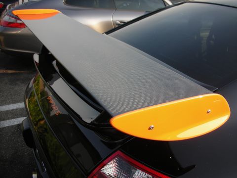 1998 Ford Crown Victoria - A black Porsche with a carbon fiber rear wing bright orange end plates is parked next to another car.