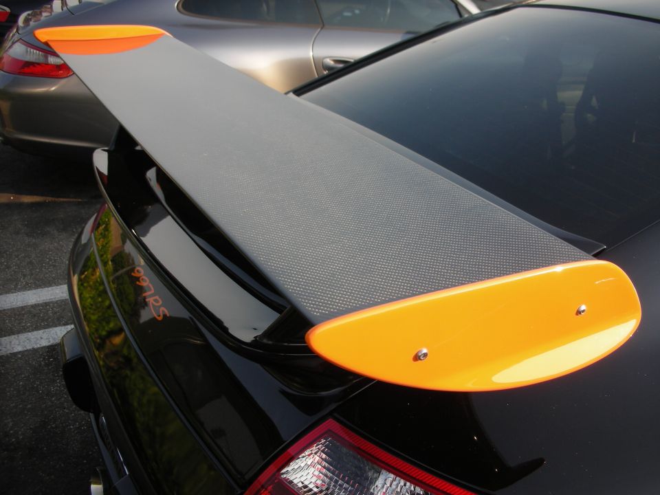 Black Porsche with carbon fiber rear wing with orange end plates. Text '997RS' visible