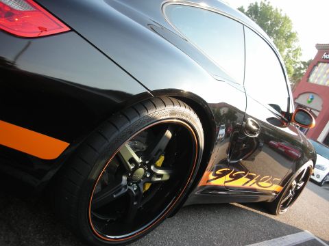 1998 Ford Crown Victoria - A black Porsche 997 with distinctive orange racing stripes and custom wheels is parked on asphalt.