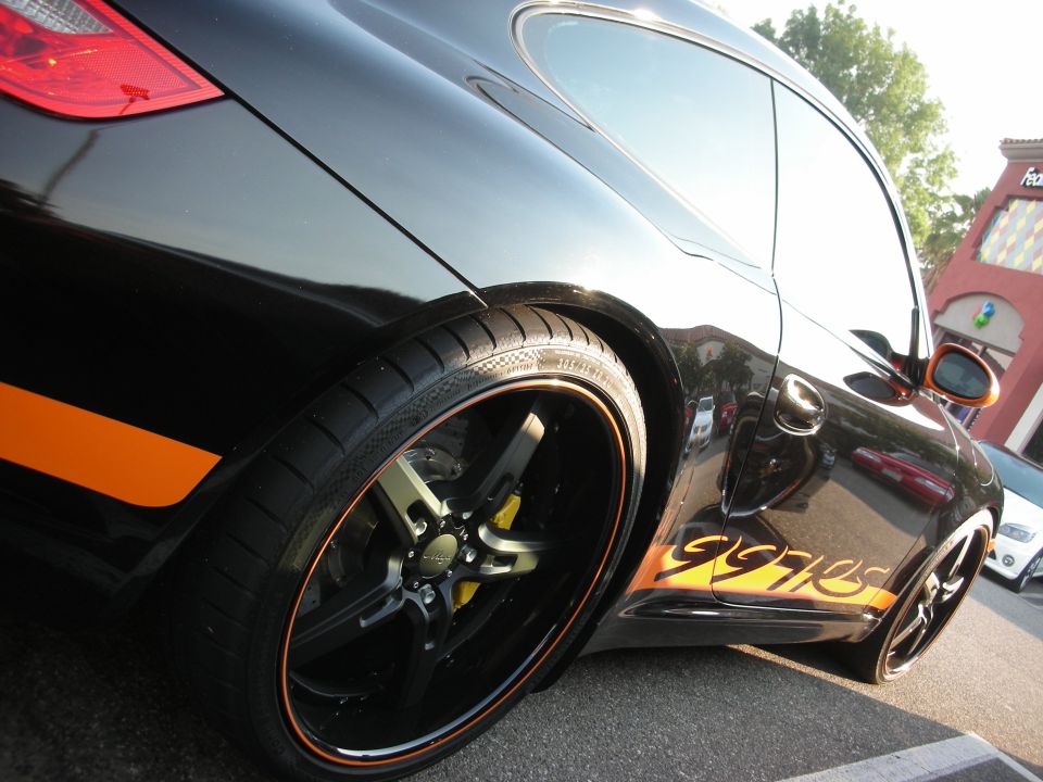 Black Porsche 997 with orange racing stripes on the side, custom wheels, and yellow brake calipers