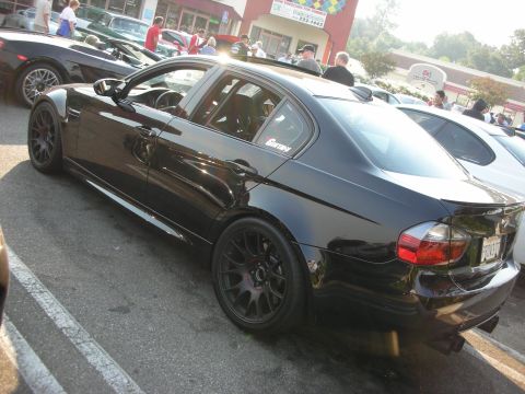 1998 Ford Crown Victoria - A black BMW sedan is parked in a lot with other vehicles and people in the background.