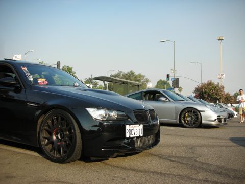 1998 Ford Crown Victoria - A line of cars, including a black BMW M3 and a silver Porsche, are parked on the street under a clear sky.