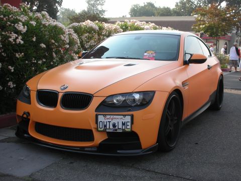 1998 Ford Crown Victoria - Orange BMW coupe parked next to flowering bushes, front view.