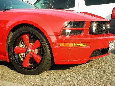 1998 Ford Crown Victoria - A red Ford Mustang is parked next to other vehicles, showing its distinctive grille and headlights.