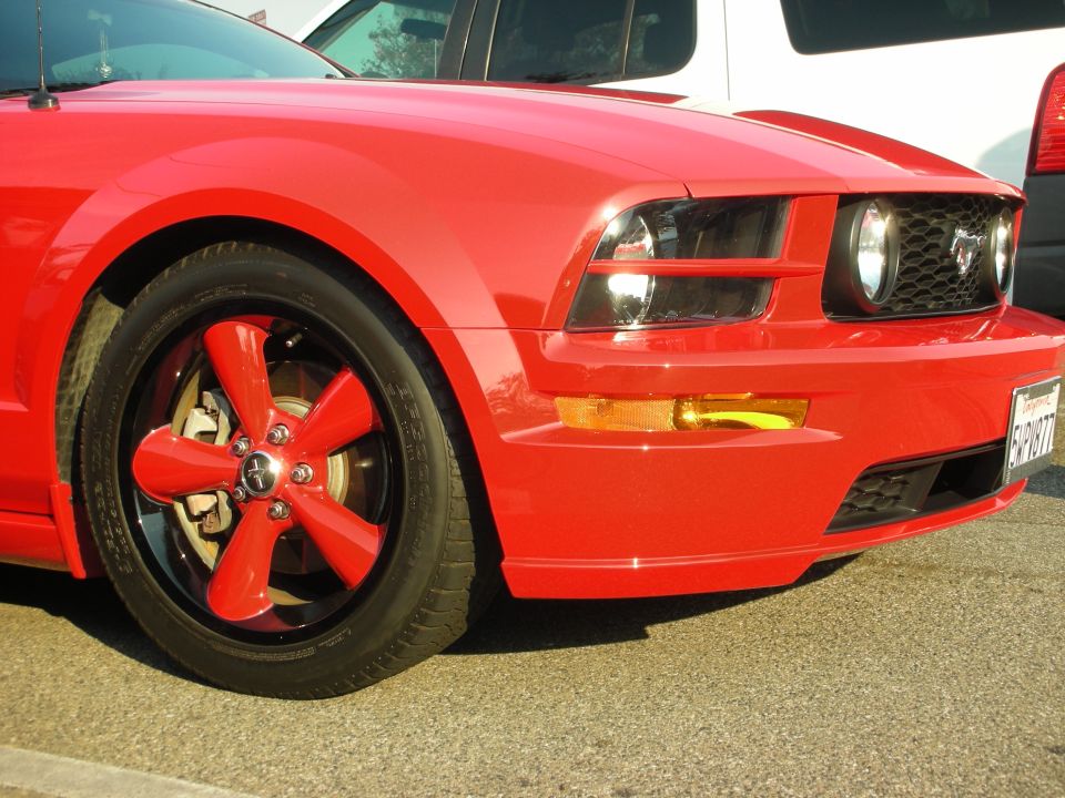 Red Ford Mustang with custom red five-spoke wheels and black rims, front passenger side view
