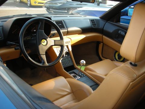 1998 Ford Crown Victoria - The interior of a sports car features tan leather seats and a gated manual shifter, with other vehicles visible through the windows.