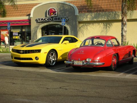 1998 Ford Crown Victoria - Two classic cars, a red coupe and a yellow coupe, are parked in front of a Taco Bell restaurant.