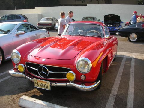 1998 Ford Crown Victoria - A red 1957 Mercedes-Benz 300SL Gullwing parked at a car meet, with other vehicles visible in the background.
