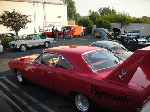 1998 Ford Crown Victoria - A red Plymouth Superbird, identifiable by its distinctive rear wing and side lettering, is parked among other vehicles at a car meet.