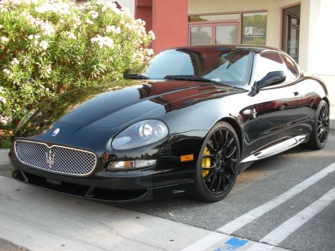 1998 Ford Crown Victoria - A black Maserati coupe is parked in a lot, a distinctive trident grille and black alloy wheels.