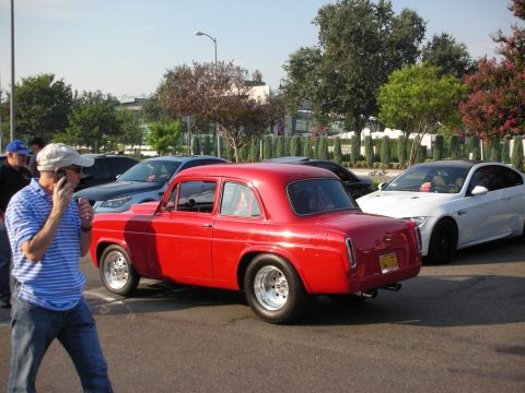 1998 Ford Crown Victoria - A red classic sedan is parked in a lot with other vehicles, while a man walks by talking on his phone.