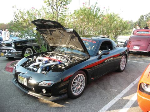 1998 Ford Crown Victoria - A black Mazda RX-7 is parked with its hood open, revealing the engine bay and a red racing banner visible through the windshield.
