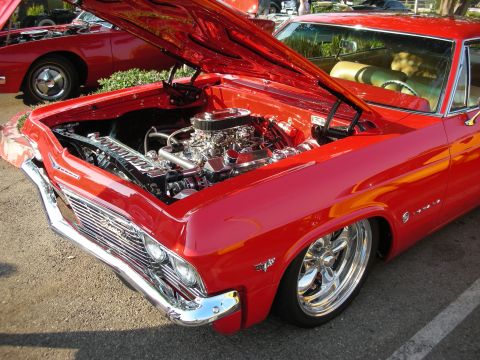1998 Ford Crown Victoria - A bright red 1965 Chevrolet Impala is displayed with its hood open, revealing a polished engine and a tan interior, with another red car vi…