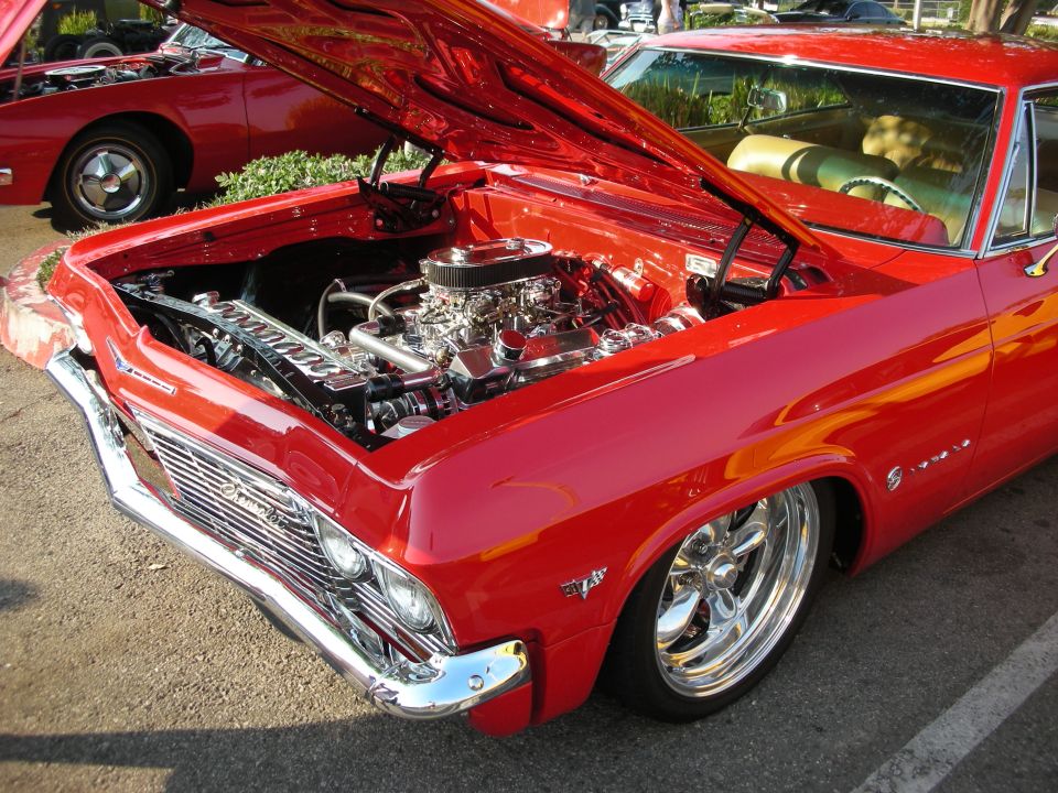 Red 1965 Chevrolet Impala with hood open, showing chrome engine and tan interior