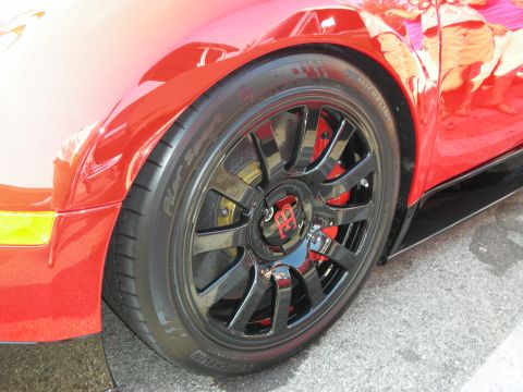 1998 Ford Crown Victoria - Close-up of a red sports car's front wheel and fender, showing custom black rims and red brake calipers.