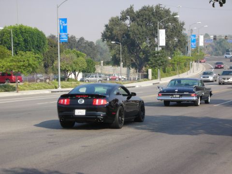 1998 Ford Crown Victoria - A black Ford Mustang drives down a street with other vehicles present.