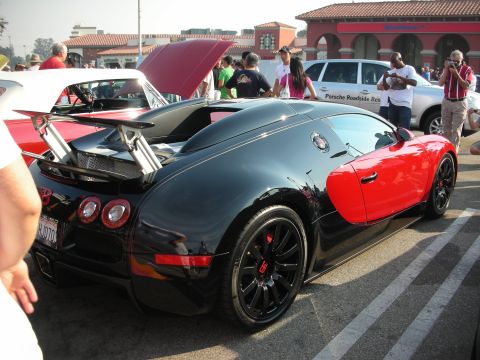 1998 Ford Crown Victoria - A black and red Bugatti Veyron is parked at a car meet, displaying its distinctive rear spoiler and dual-tone paint scheme.