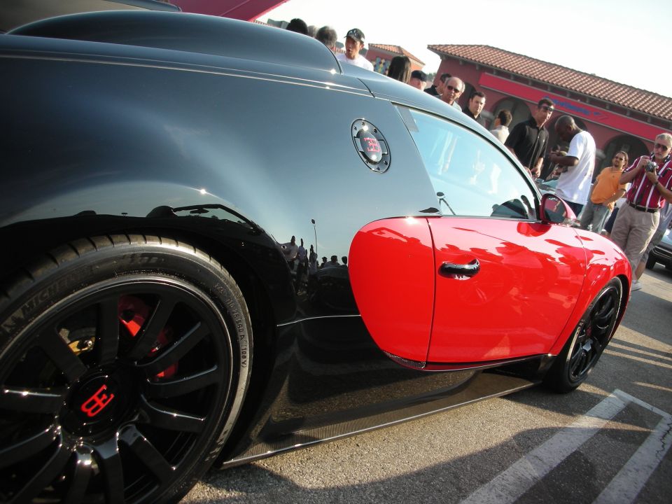 Bugatti Veyron with black body and red door, parked outdoors with people around