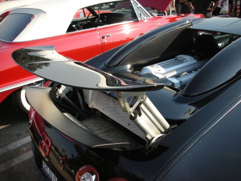 1998 Ford Crown Victoria - A close-up view of a black sports car's rear spoiler and engine compartment, parked next to a red convertible.