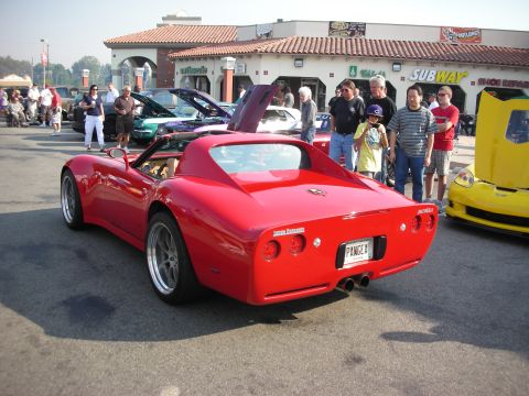 1998 Ford Crown Victoria - A red sports car is parked at a car meet, with a yellow Corvette nearby.