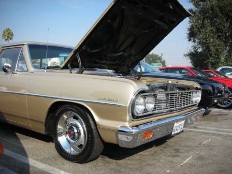1998 Ford Crown Victoria - A classic gold Chevrolet Chevelle is parked with its hood up, showing off its engine bay.