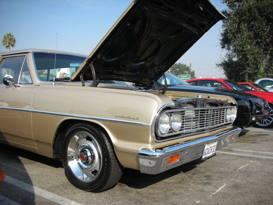 Gold 1960s Chevrolet Chevelle with hood open, parked in lot with other cars