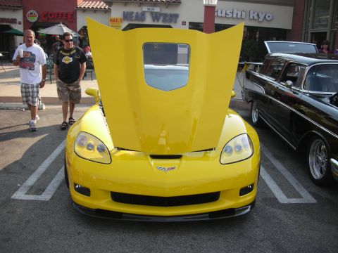 1998 Ford Crown Victoria - A yellow Chevrolet Corvette C6 is parked with its hood open, alongside a vintage black car.