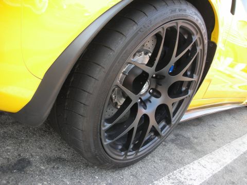 1998 Ford Crown Victoria - A close-up shot focuses on the wheel and fender of a yellow sports car, highlighting its performance tire and custom rim.