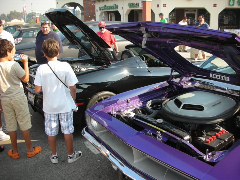 Purple muscle car with hood open, showing engine. Black muscle car also with hood open. Kids looking at cars
