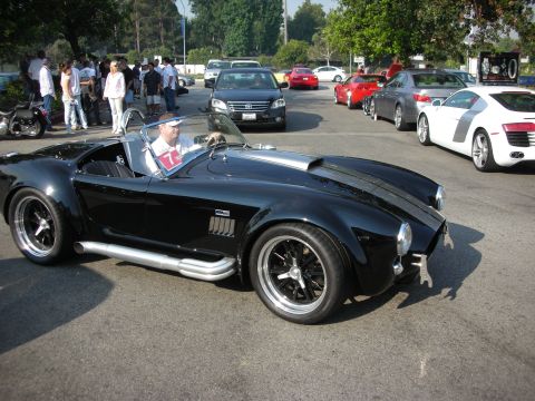 1998 Ford Crown Victoria - A black AC Cobra replica is parked among other vehicles at an outdoor gathering.