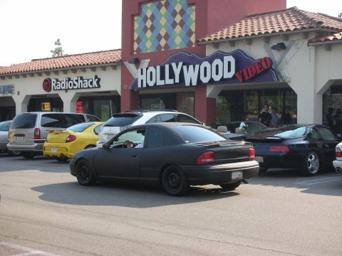 1998 Ford Crown Victoria - A black coupe is parked in front of a Hollywood Video store, with other vehicles visible.