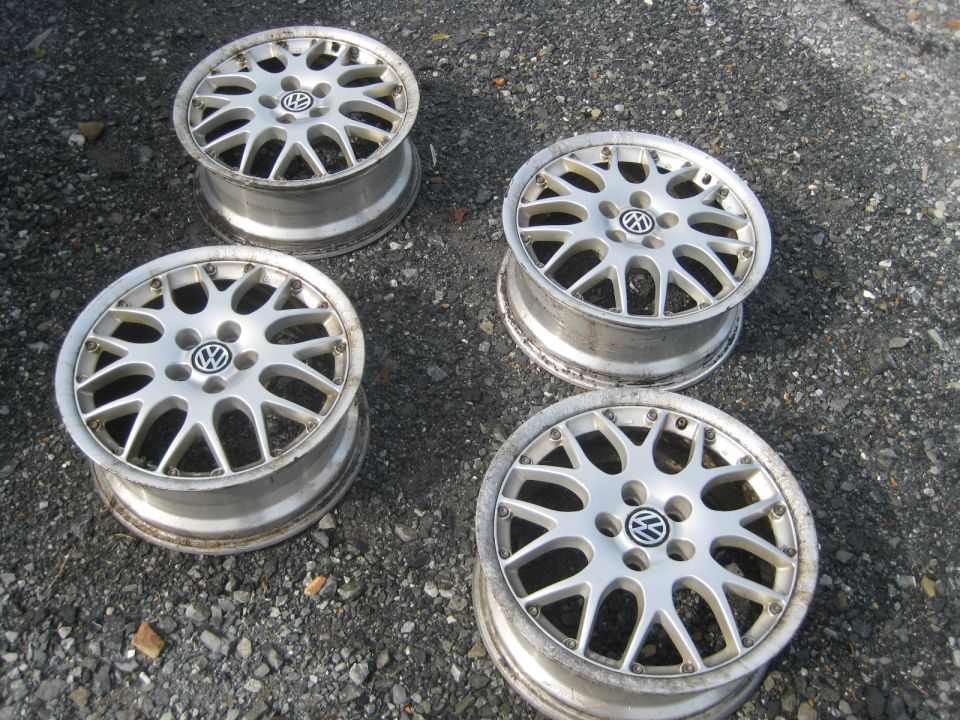 Four silver Volkswagen alloy wheels with the VW logo in the center, resting on a gravel surface