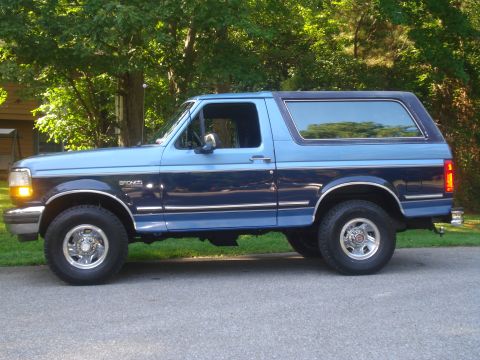 1992 Ford Bronco - This blue 1992 Ford Bronco is shown from its side profile against a backdrop of trees and a house.