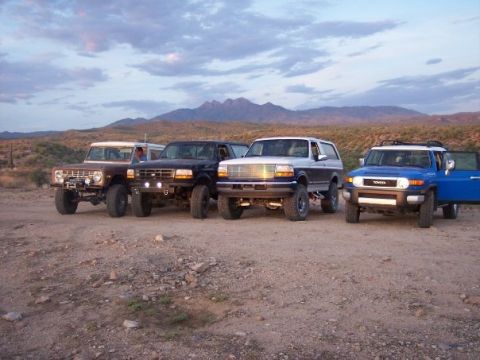 1996 Ford Bronco - A group of off-road vehicles are parked in a desert landscape with mountains in the background.