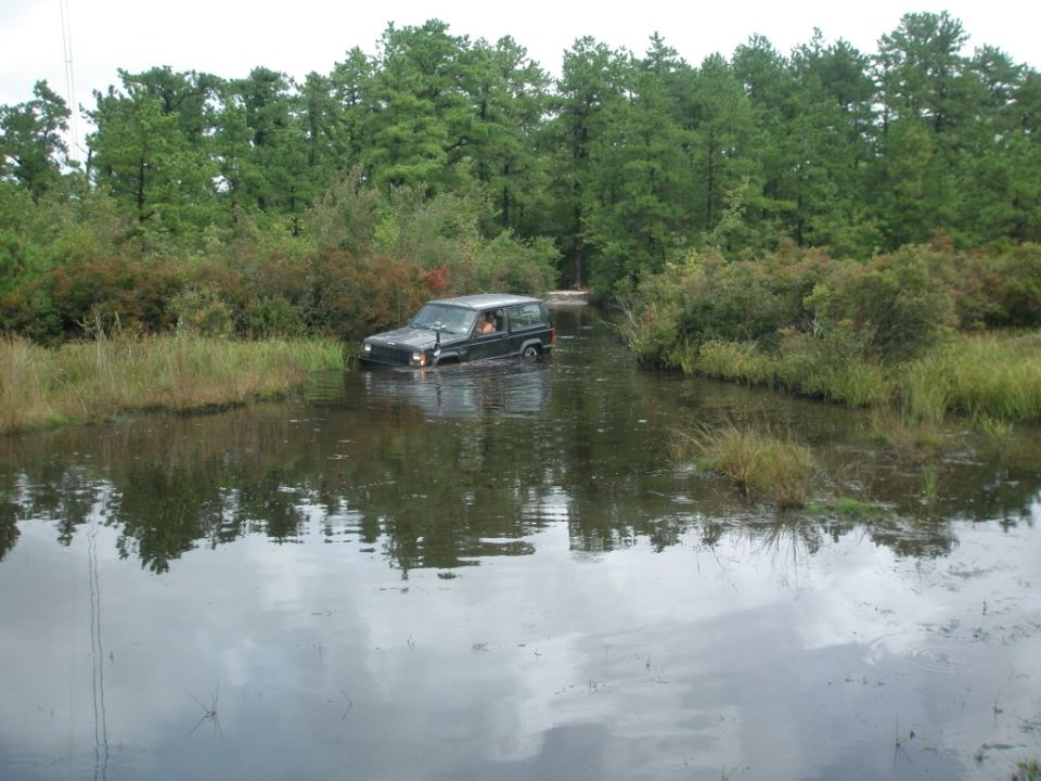 1993 Jeep Cherokee driving through shallow water with trees in background