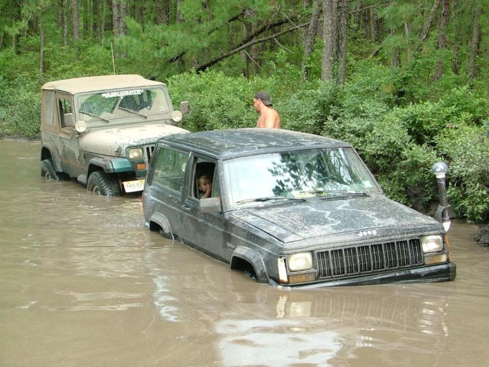 Two Jeeps stuck in muddy water, one is a dark Cherokee and the other is a tan Wrangler