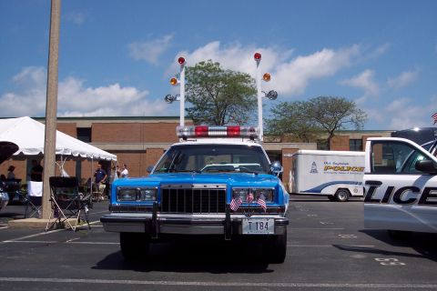 2001 Ford Crown Victoria - A police car with a light bar and flags is parked in a lot, with another police vehicle nearby.